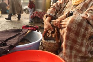 Woman wearing traditional Pheran with firepot(Kangir) for heating, selling fish during cold weather days.