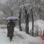 Man wearing Pheran with umbrella to cover his body from snow fall.