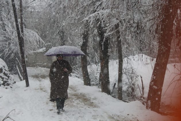 Man wearing Pheran with umbrella to cover his body from snow fall.