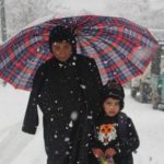 Children Under the umbrealla posing for the camera in snowfall.
