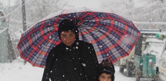 In Pictures: Life Amid Snow In Kashmir Children Under the umbrealla posing for the camera in snowfall.