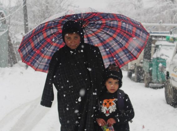 Children Under the umbrealla posing for the camera in snowfall.