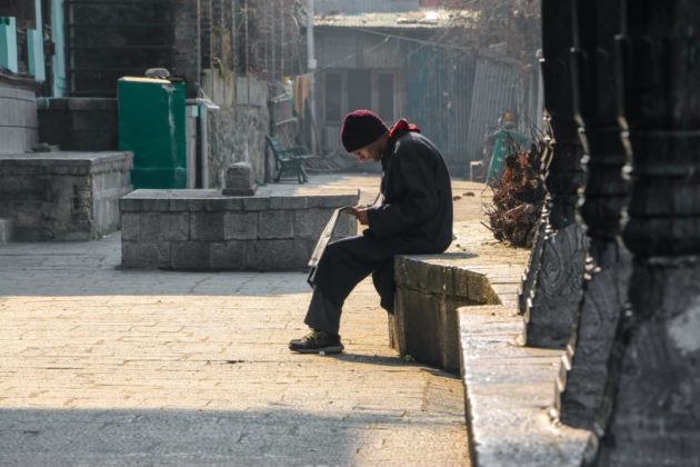 Man reading newspaper while soaking sun in the serene environment of Khanqa-E-Maula.