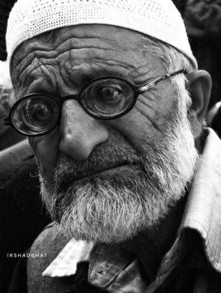 An old man with glasses on, trying to pose for me as I am trying to find the best possible angle to get a good portrait.